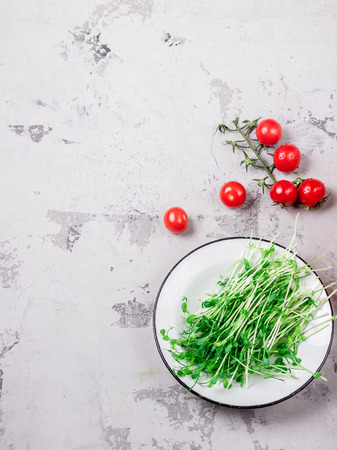 Fresh greens on white plate and tomatoes. White stone background.の写真素材