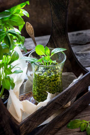 Basil pesto sauce in glass and wooden box with fresh basil on old wooden background. Style rustic. Selective focus.の写真素材