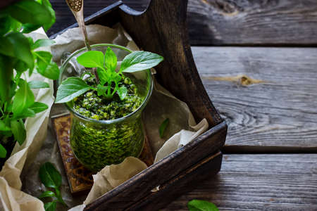 Basil pesto sauce in glass and wooden box with fresh basil on old wooden background. Style rustic. Selective focus.の写真素材