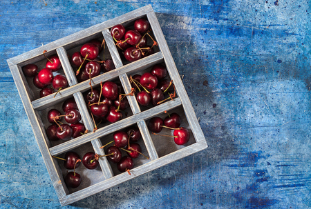 Wooden box with sweet cherry on blue background. Place for text.の写真素材