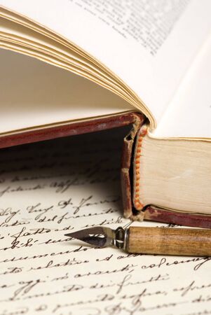An old book lies open with a pen on top of a hand written document in calligraphy.