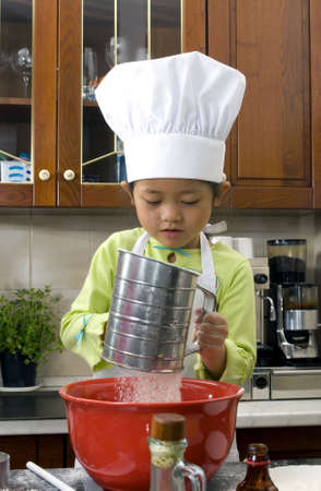 Two young sisters have fun in the kitchen making a mess....I mean making cookies. Education, learning, cooking, childhoodの写真素材