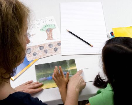 A young girl learns to write with the help of a teacher.