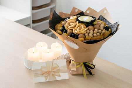 Elegant bouquet of dried fruits, nuts, and honey jar wrapped in kraft paper, accompanied by white decorative candles and a gift card on a wooden table. Perfect for gifts, celebrations, or special occasionsの写真素材