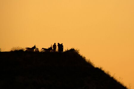 Silhouette of two motorbikes and bikers on a hill at sunset                 の写真素材