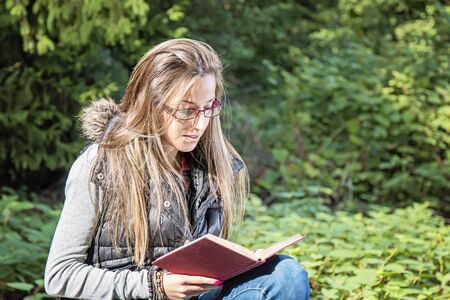 Portrait of attractive young girl with book in a park