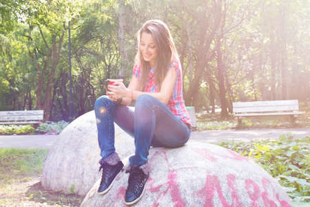 Beautiful young woman with a red cup drinking coffee in a morning parkの写真素材