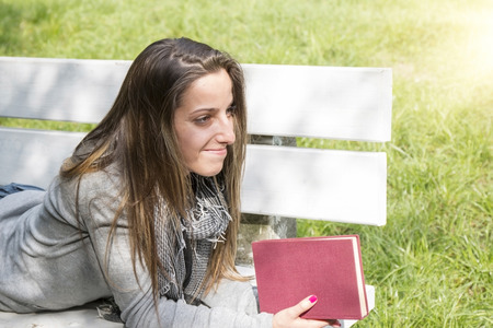 Young woman reading a book on a park bench in a lovely sunny dayの写真素材