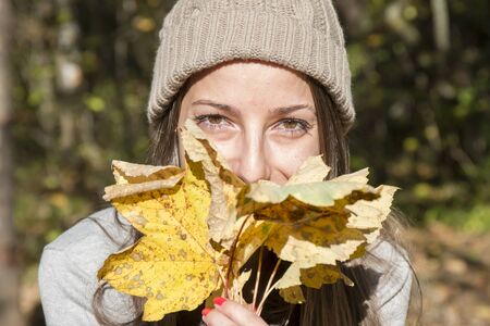 Young woman with hat playing with autumn maple leaves in the park
