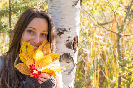 Young woman with red fruits and yellow leaves in hand in autumn parkの写真素材