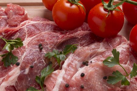 Fresh raw pork chop meat on cutting board with tomatoes, parsley and black pepperの写真素材