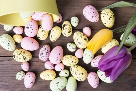 Colorful Easter eggs on bowl and tulips on a wooden tableの写真素材