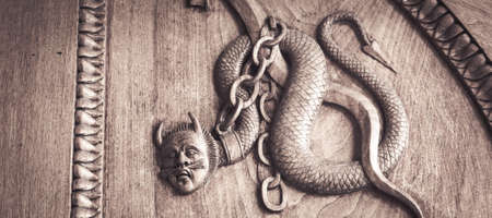 Devil snake symbol. Fantasy magic creature on an old door, 12th Century Abbey, Italy.の写真素材