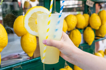 Caucasian hand with healthy fresh lemonade during summer with lemons backgroundの写真素材