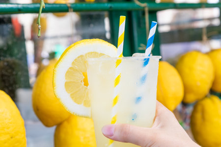 Caucasian hand with healthy fresh lemonade during summer with lemons backgroundのeditorial素材