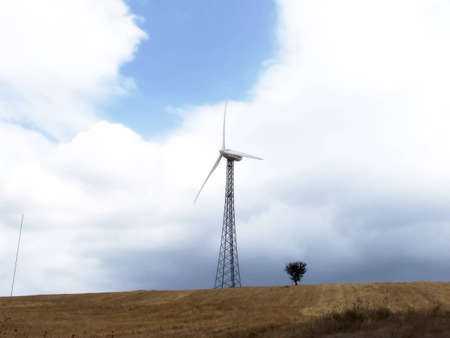 A windmill for electic energy in a country field with cloudly sky