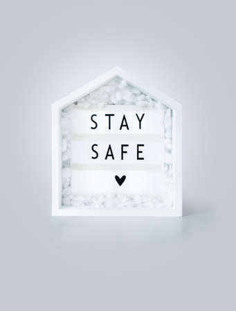 stay safe lettering on a lightbox with wooden house, concept of self quarantine as preventative measure against virus.の写真素材