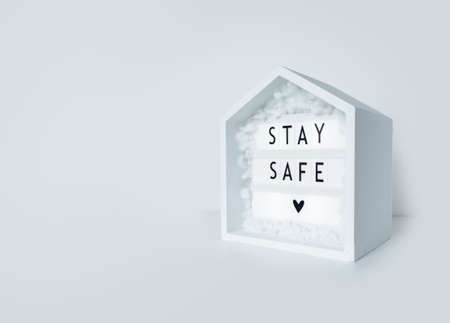 stay safe lettering on a lightbox with wooden house, concept of self quarantine as preventative measure against virus.の写真素材