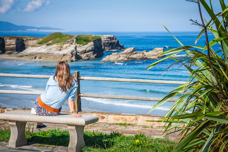 Young woman sitting on bench facing the seaの写真素材
