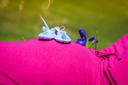 Pregnant woman lying on a grass with baby shoes on her belly