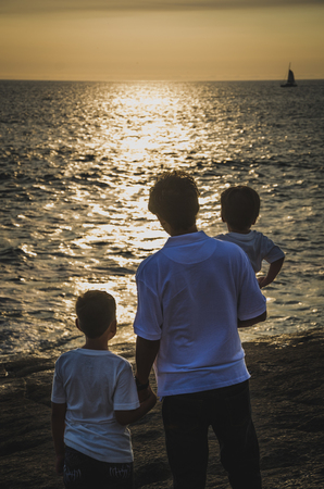 Father with children facing the sea at sunsetの写真素材