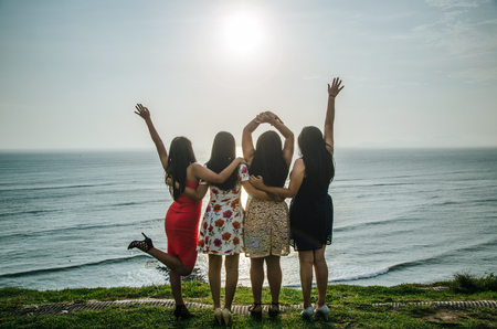 Girls in front of the sunset raising their handsの写真素材