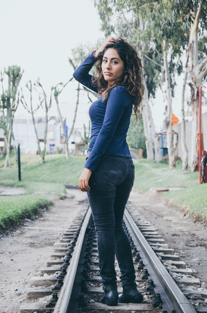 Young sexy girl with long hair in jeans on a railway. Alluring woman looking at cameraの写真素材