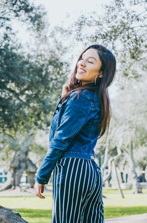 Young happy brunette woman in jeans jacket in the summer park
