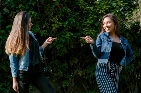 Cheerful friends are gossiping in the park. The girls are pointing with their finger and laughing....