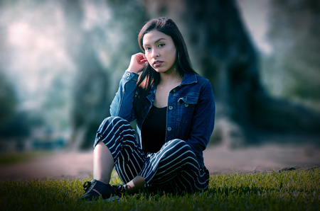 Portrait of an attractive, young and attractive brunette woman sitting on the lawn. She leans back and relaxes while smiling.の写真素材