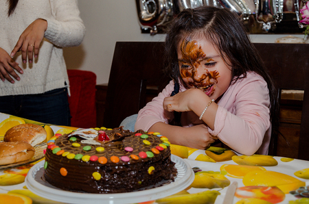 6 year old girl celebrating her birthday by putting her face inside the chocolate cakeの写真素材