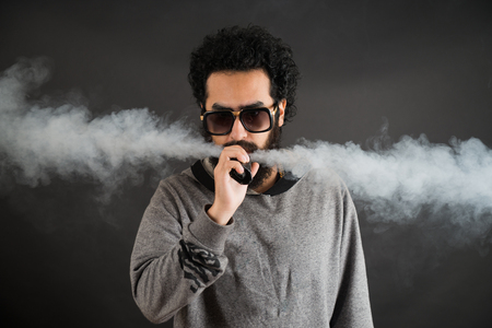 Vaping man holding a mod. A cloud of vapor. Black background. Vaping an electronic cigarette with a lot of smoke. Vape conceptの写真素材