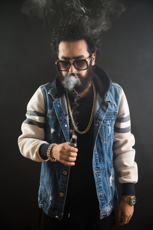 Young man with beard and sunglasses vaping an electronic cigarette. Vaper hipster smoke vaporizerの写真素材