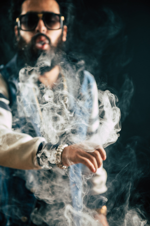Young man with beard throwing a cloud of steam. Black background. Vaping an electronic cigarette...