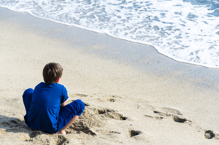A boy looking at the sea with his back to the camera. Child looking at the sea on the beachの写真素材