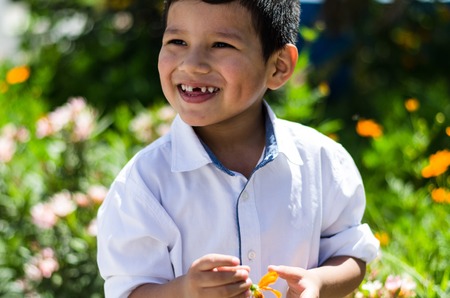 small baby boy holding a daisy in his hand and laughing in the field of flowersの写真素材