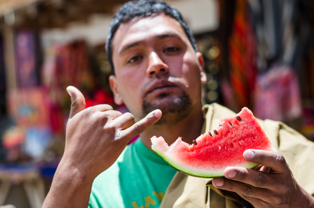 Elegant dark-skinned young man refreshing himself on summer day, eating ripe watermelon.の写真素材