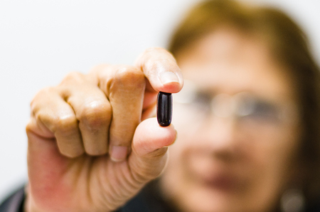 Adult woman showing a pill in the foreground, seniors health concept .の写真素材