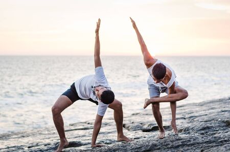 Two friends practicing Yoga on the edge of the ocean at sunset, Yoga or meditation conceptの写真素材
