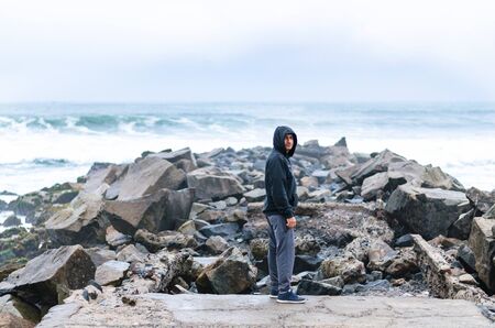 Man standing on the rock in the middle of the ocean. Tourist standing at the edge of the sea looking at the cameraの写真素材
