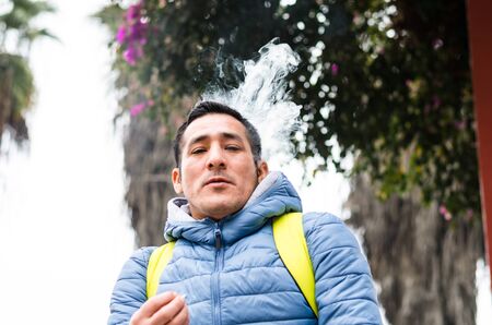 A man with a backpack smoking and smoke coming out of his mouthの写真素材