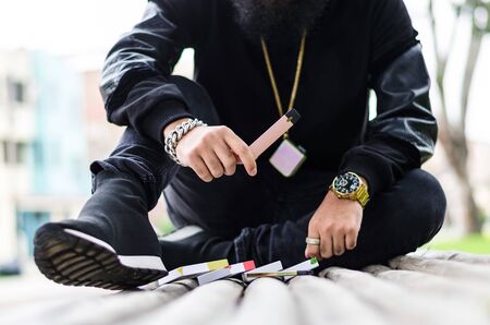 Man with a beard smokes an electronic cigarette sit on a bench in the parkの写真素材