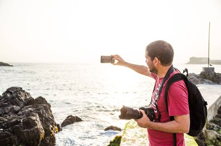 A male photographer taking a selfie on a sunny day at the beachの写真素材