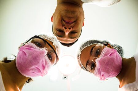 Portrait of three surgeons at work, operating in uniform, looking at the cameraの写真素材