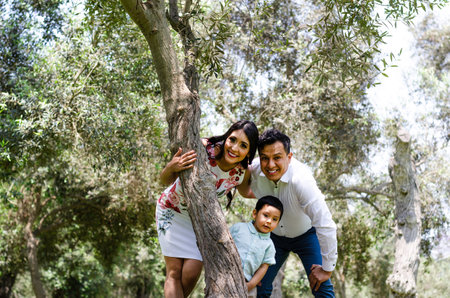 Happy family with man, woman and child leaning on tree in city park. Copy spaceの写真素材