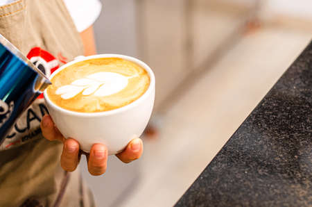 Hands of a Peruvian barista creates latte art in coffee shop, food and drink concept