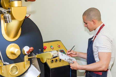 Mans hands roasting coffee aromatic coffee beans over a modern machine used for roasting beans.