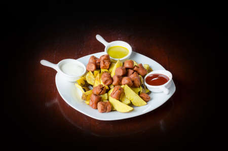 Salchipapa, peruvian grilled and sliced fresh pork sausage, potato fry on black background.