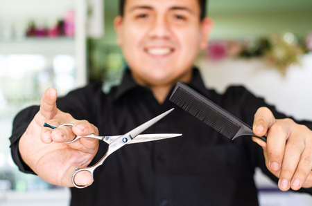 Portrait of an attractive barber holding scissors and comb in his hand.の写真素材