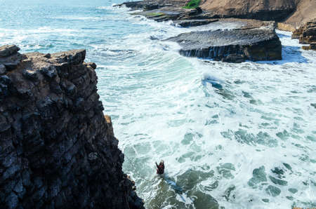 Man dressed as a friar throws himself off a cliff and head into the ocean at sunset.の写真素材